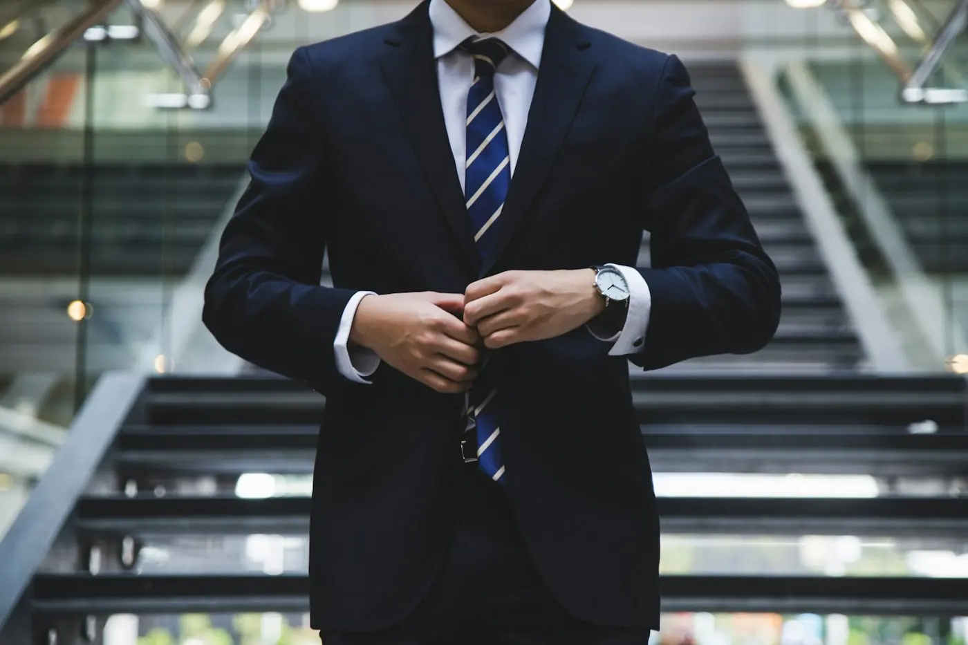 A man in a navy suit buttoning his jacket