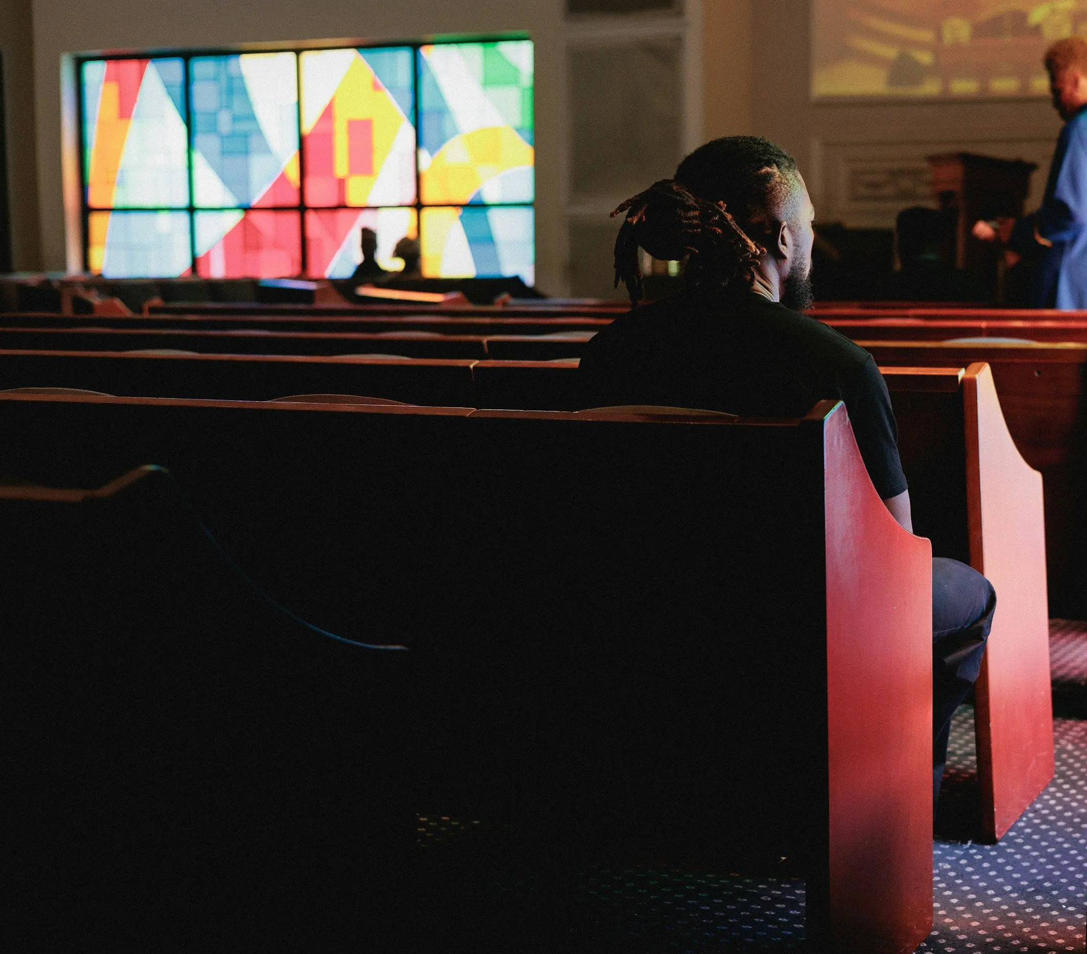 A worshipper seated in a quiet church pew beneath stained glass