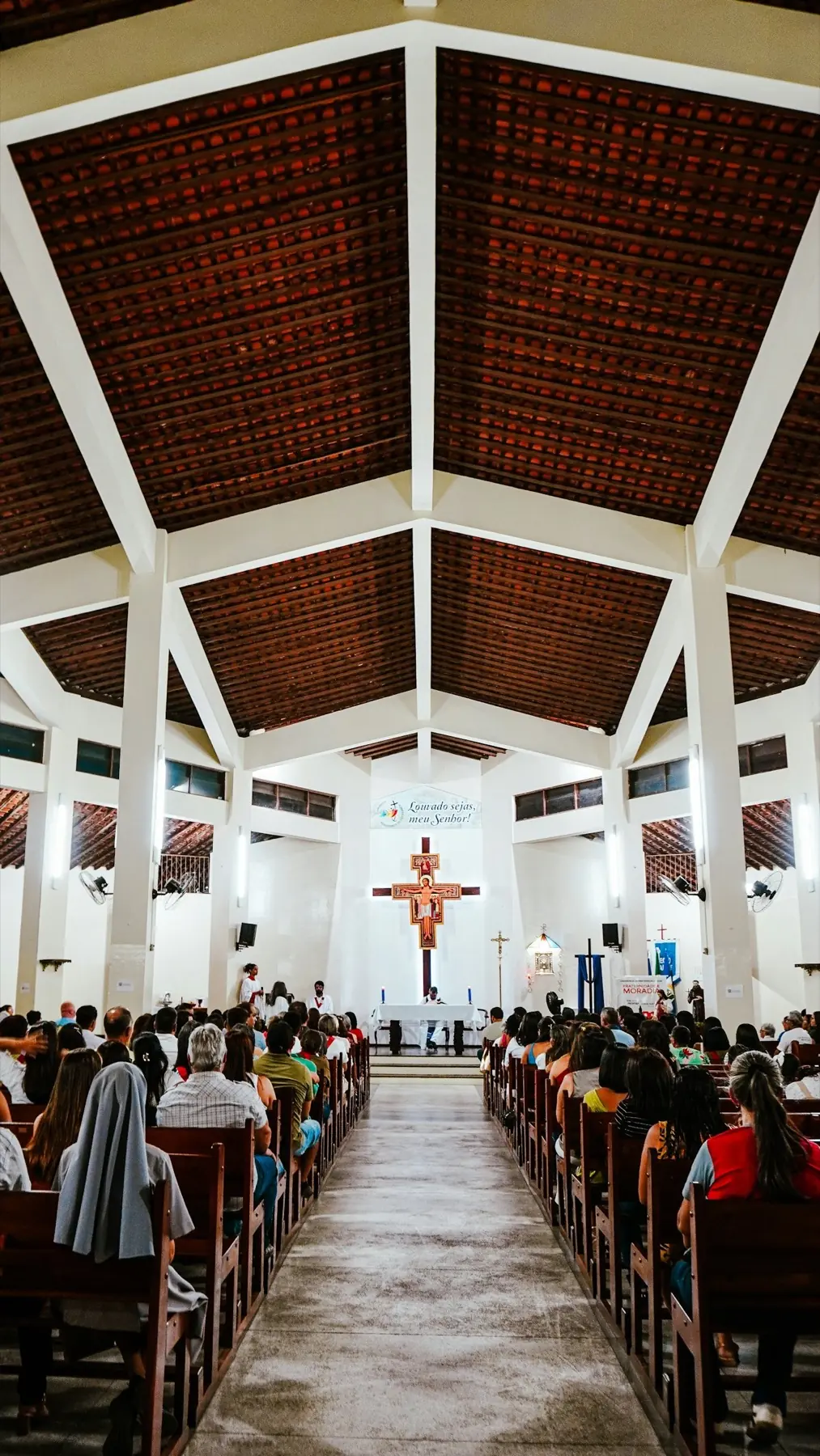 A congregation seated facing the cross in a bright sanctuary